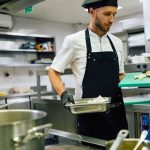 Cocinero en cocina de restaurante con bandejas en las manos