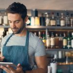 Hombre con delantal en un restaurante sostiene una tablet en sus manos